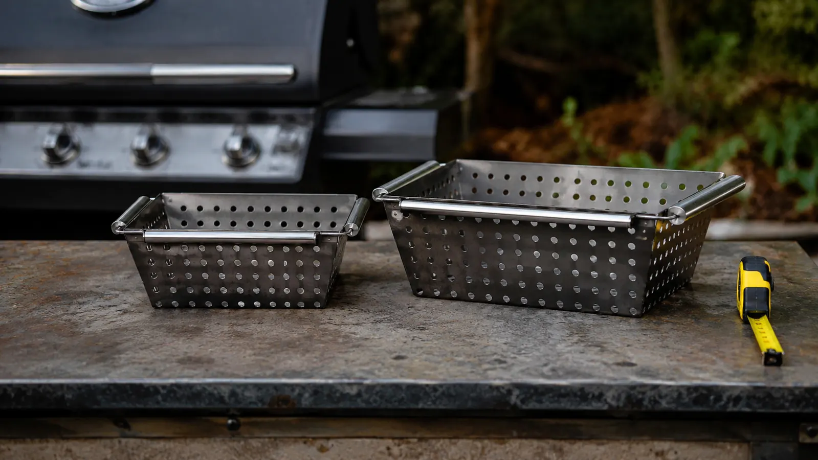 Two grill baskets of different sizes sitting side by side on a workbench for comparison