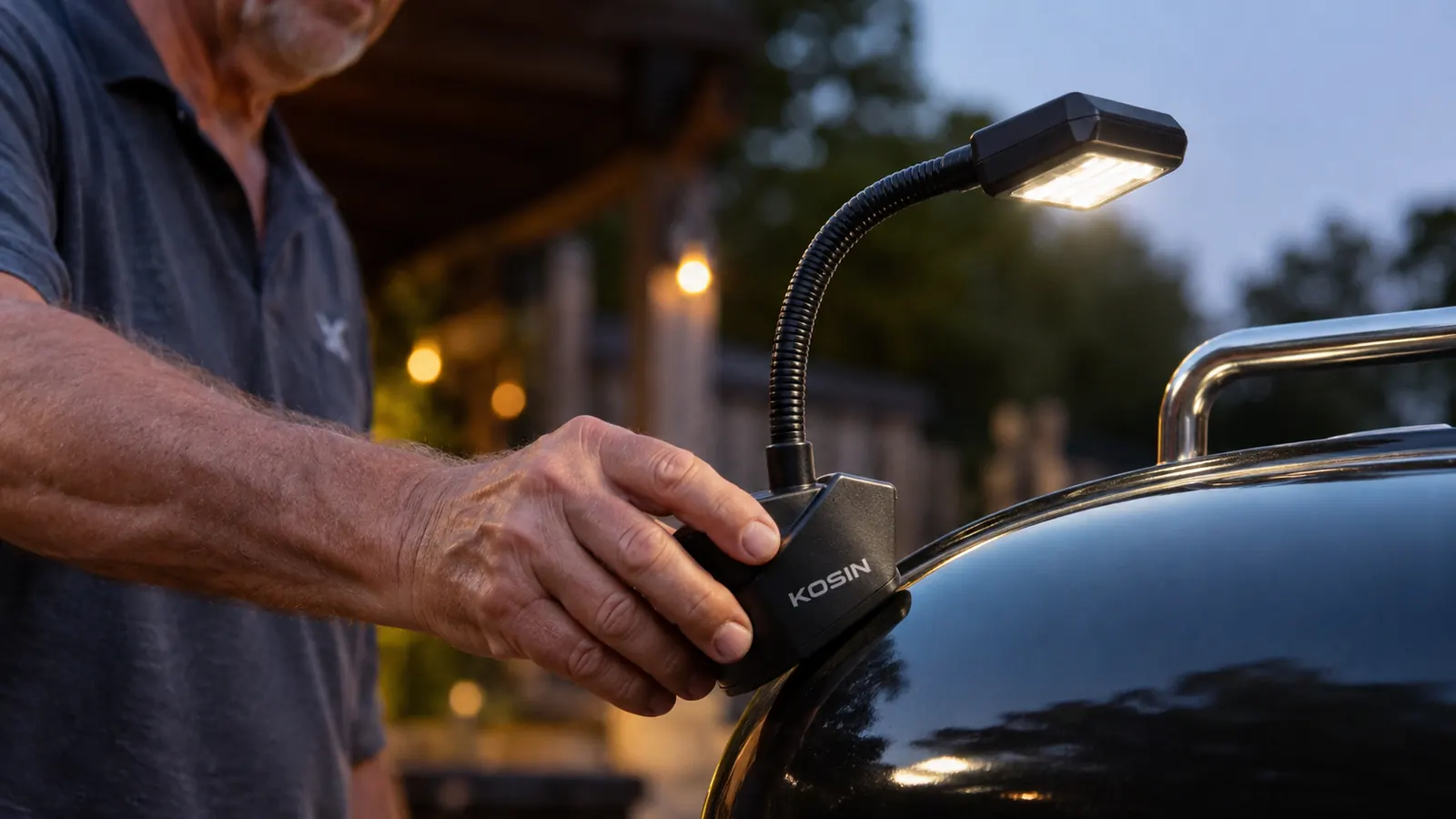 Close-up of a hand attaching the KOSIN magnetic grill light's base to the metal lid of a gas grill