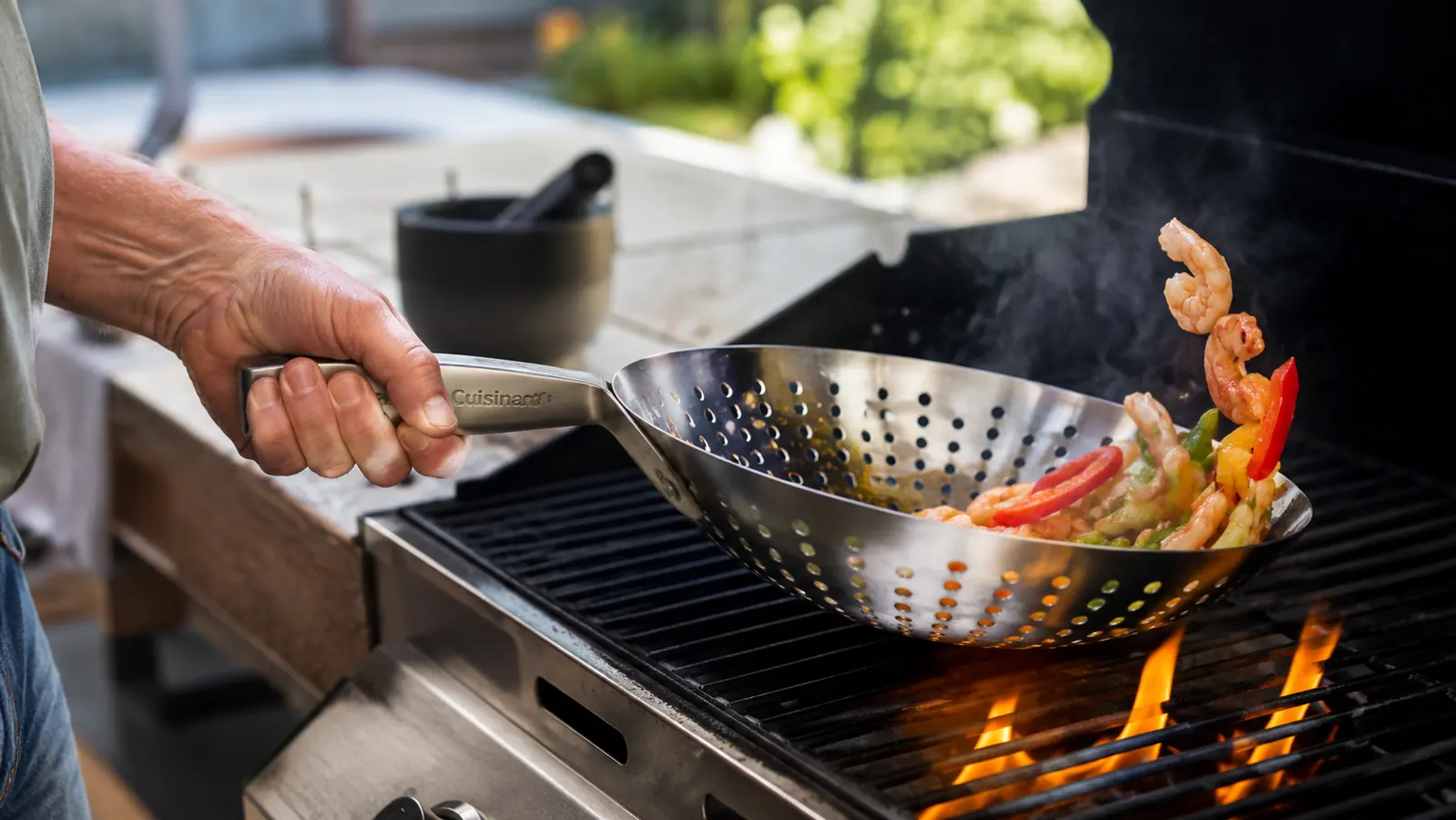 A hand shaking the Cuisinart Grill Wok over the grill grate to toss the vegetables