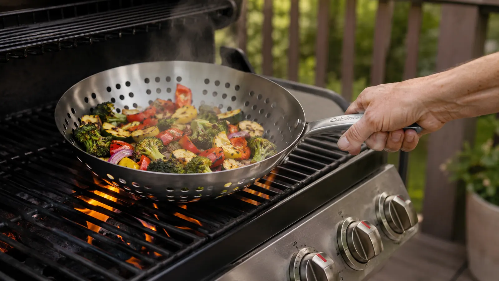 Hand shaking a Cuisinart grill wok full of sliced peppers and onions over an open grill flame