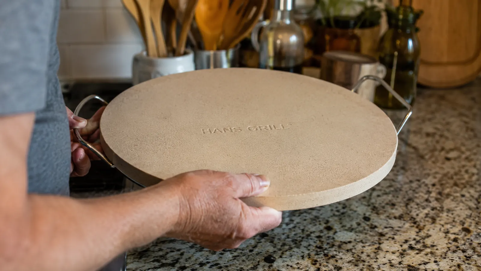 Close-up of hands lifting the Hans Grill Pizza Stone PRO XL out of its box, showing its thickness and weight