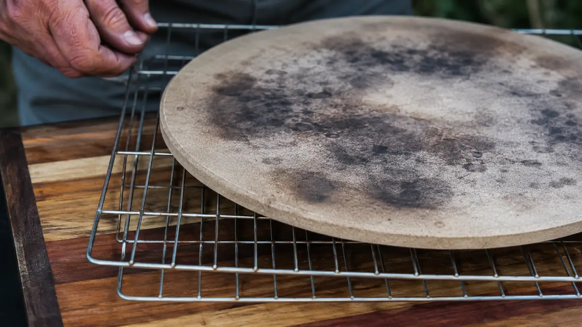The underside of a well-used pizza stone showing permanent gray-black smoke discoloration in a ring pattern