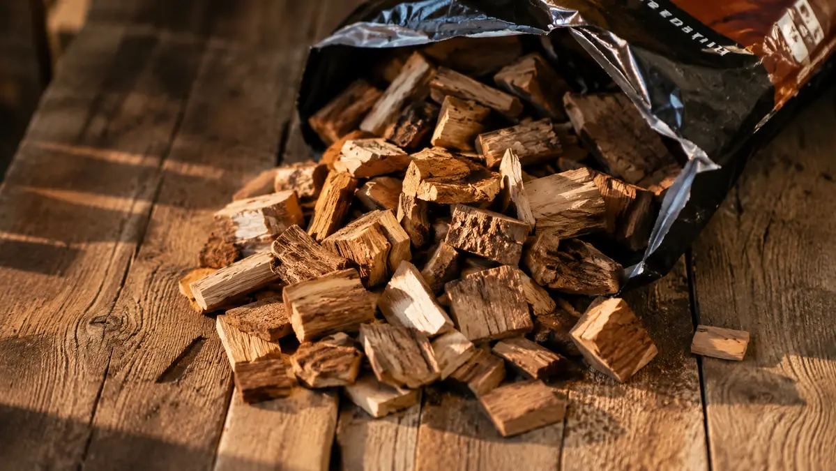 Close-up of Weber hickory wood chunks spilled out of the bag onto a wooden table, showing mixed chunk sizes and bark fragments