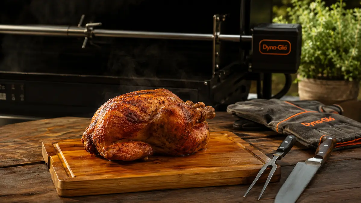 A rotisserie-cooked whole chicken resting on a cutting board with crackling golden skin and visible juices