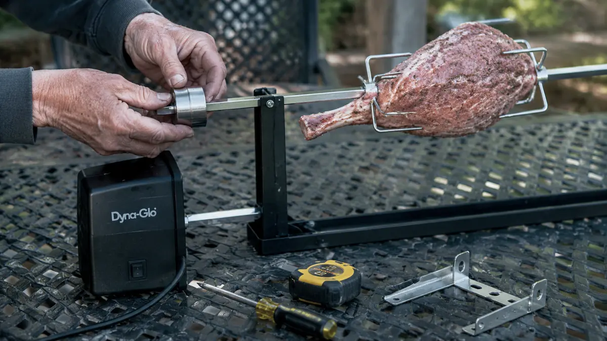 Close-up of a hand adjusting the counterweight on a rotisserie spit rod to balance an unevenly shaped roast